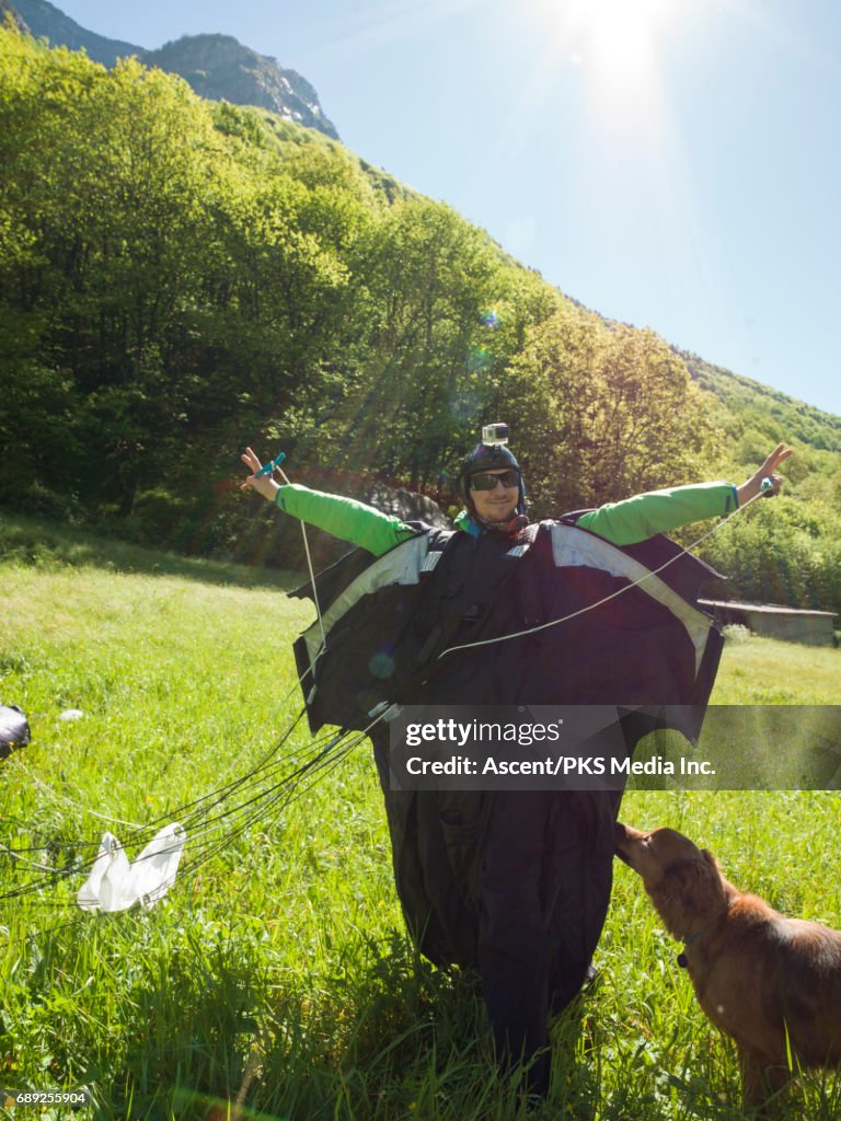 Wingsuit flyer lands in green meadow, mountains