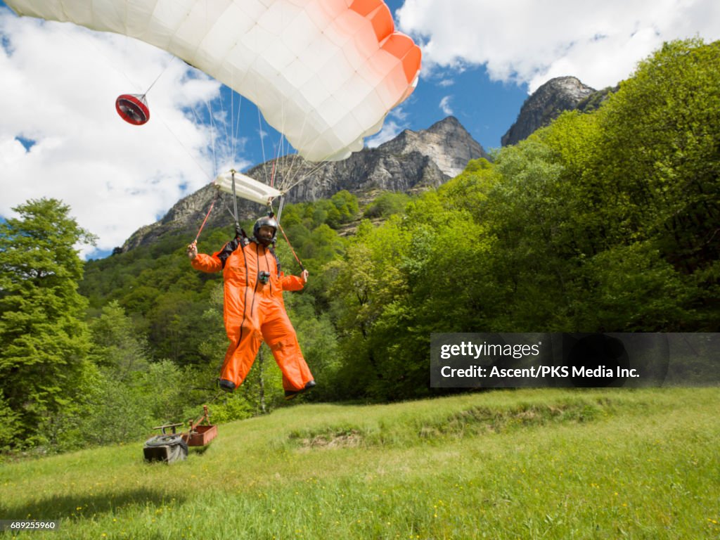 Wingsuit flyer lands in green meadow, mountains