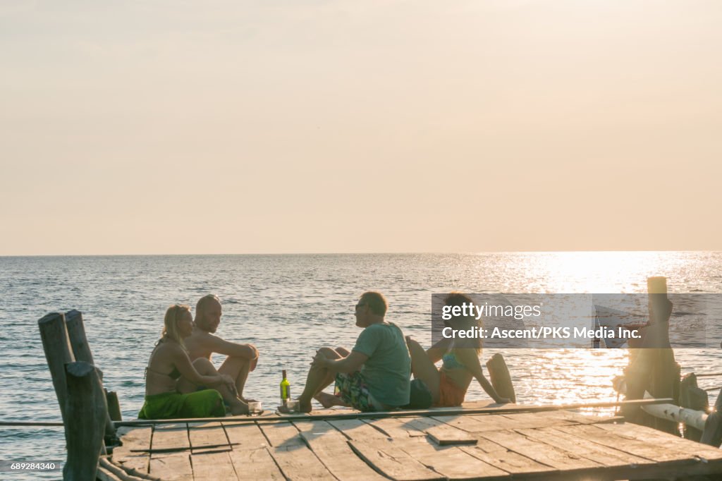 Mature couples enjoy wine on wooden deck at sunset