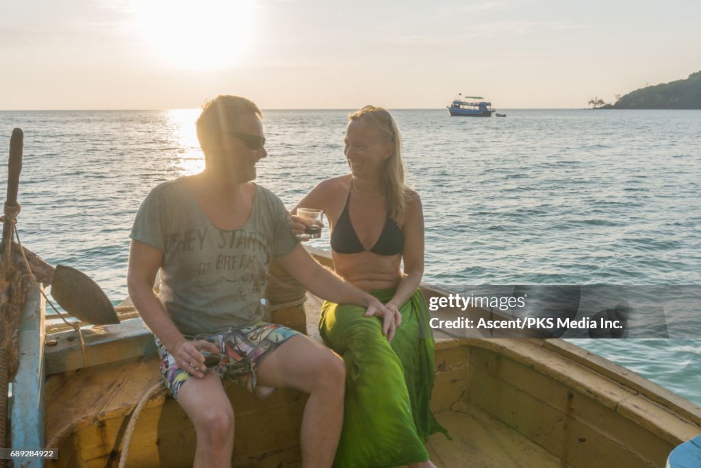 Mature couple enjoys wine on wooden deck at sunset