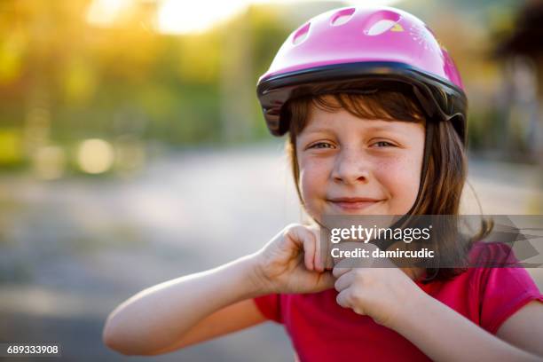 happy cute girl putting cycle helmet on - work helmet stock pictures, royalty-free photos & images