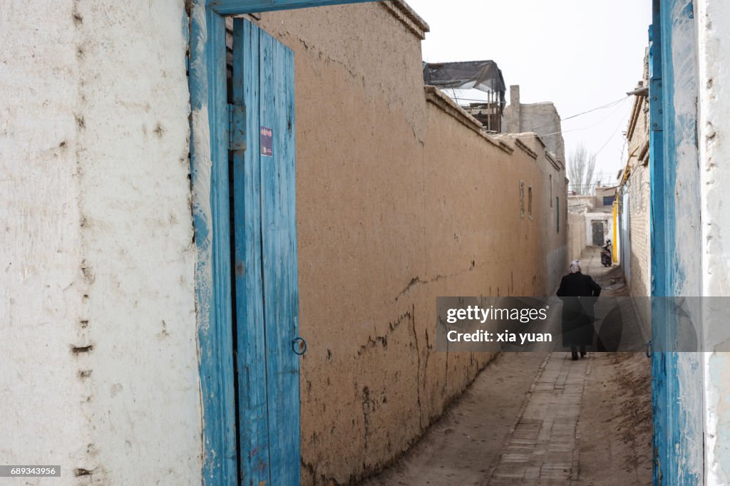Senior woman walking along alley admist mud-brick houses in Kuqa,China