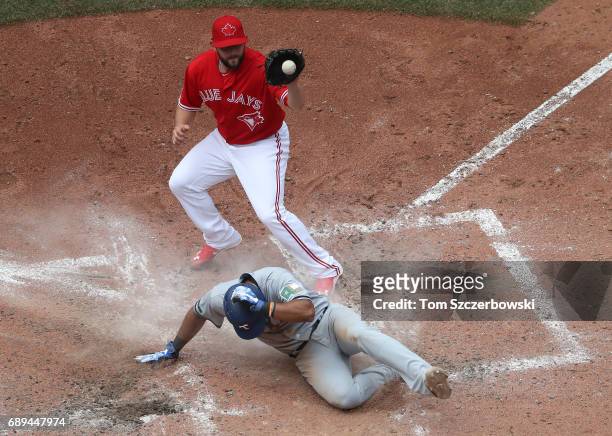 Elvis Andrus of the Texas Rangers slides across home plate as he scores on a wild pitch as Dominic Leone of the Toronto Blue Jays covers home plate...