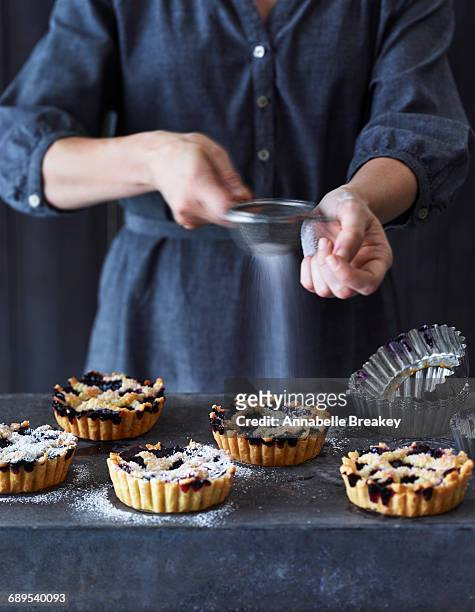 Woman Sifting Powdered Sugar Over Blueberry Tarts