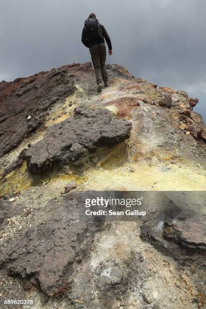 Visitor passes by rocks coloured yellow by sulphur while hiking among craters and gravel-like ash near the peak of Mount Etna on the island of Sicily...