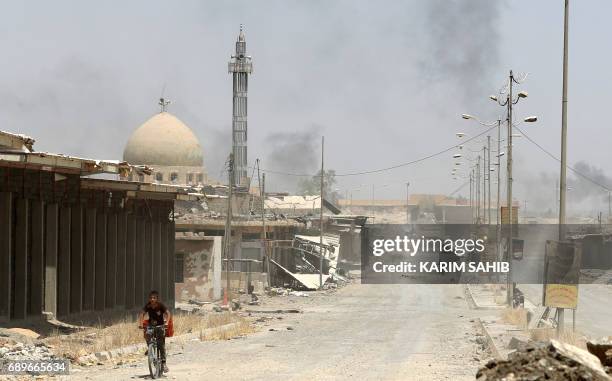 An Iraqi boy rides a bicycle in west Mosul's al-Saha neighbourhood on May 29, 2017 as smokes billows during ongoing battles by Iraqi forces to retake...