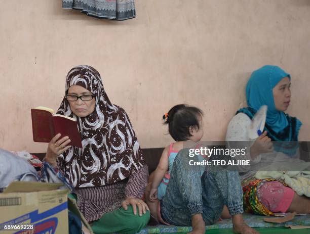 Woman reads a Quran while another family member attends to her child at an evacuation centre in Balo-i on the southern island of Mindanao on May 29,...