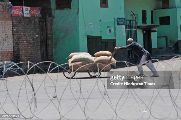 Kashmiri man pushes his handcart near barbed wire set up barricade during curfew on May 29, 2017 in downtown area of Srinagar, India. The government...