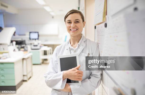 smiling female scientist holding digital tablet - woman in white lab coat stock pictures, royalty-free photos & images