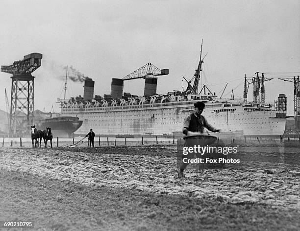 Farmers tilling the soil with horse drawn ploughs and hand sowing their seeds beside the British passenger liner for the Cunard-White Star Line, RMS...