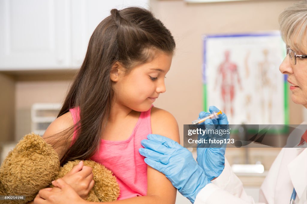 Female doctor and latin descent girl patient in pediatrician's office or clinic getting vaccination.