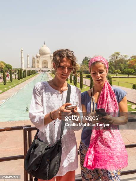 two women on a tour at the taj mahal playing with mobile phones - taj mahal selfie stock pictures, royalty-free photos & images