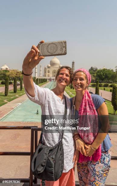 two women on a tour at the taj mahal playing with mobile phones - taj mahal fotografías e imágenes de stock