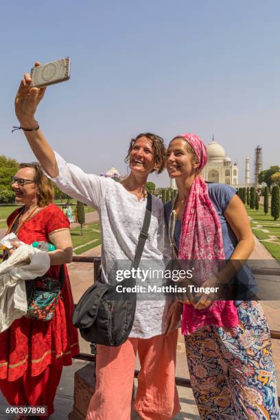 two women on a tour at the taj mahal playing with mobile phones - taj mahal selfie stock pictures, royalty-free photos & images