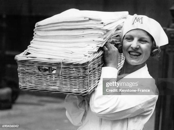 Jeune femme portant un panier plein de linges lavés et repassés, au Salon de la Blanchisserie à Londres, Royaume-Uni le 7 mai 1934.
