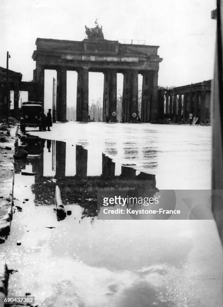 Vue de la Porte de Brandebourg se reflétant dans une flaque d'eau, à Berlin, Allemagne le 6 juillet 1945.