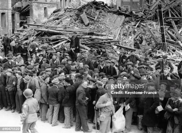 Groupe de civils allemands arrêtés pas les Forces Alliées sont réunis parmi les décombres pour recevoir nourritures et couvertures, en Allemagne le...