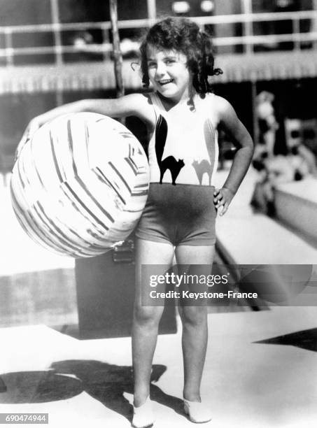 Une petite fille, élue Reine junior des baigneuses, tient un ballon sous son bras au bord de la piscine le 8 janvier 1931 à Juan-Les-Pins, France.