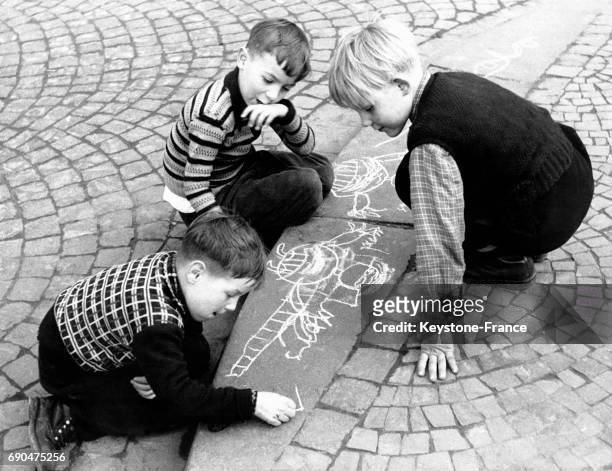 Trois garçons dessinent à la craie sur le pavé le 16 avril 1958.