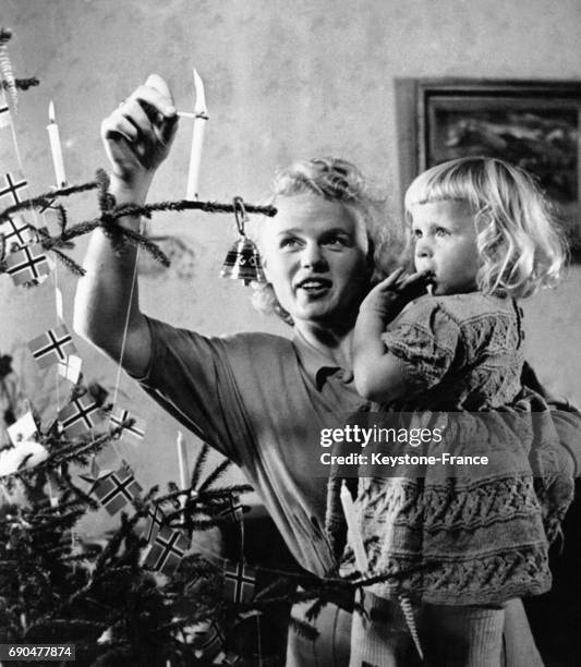 Une mère norvégienne tient sa fille dans ses bras et allume une bougie dans le sapin de Noël décoré le 16 novembre 1948 en Norvège.