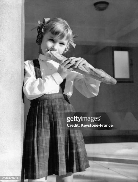 Une fillette en tenue d'écolière croque dans une baguette de pain.