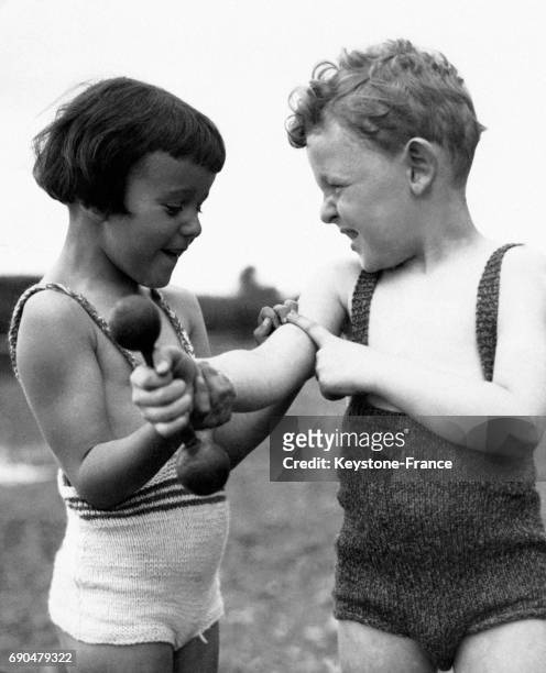 Un petit garçon montre ses muscles avec fierté à une petite fille après s'être exercé aux haltères.
