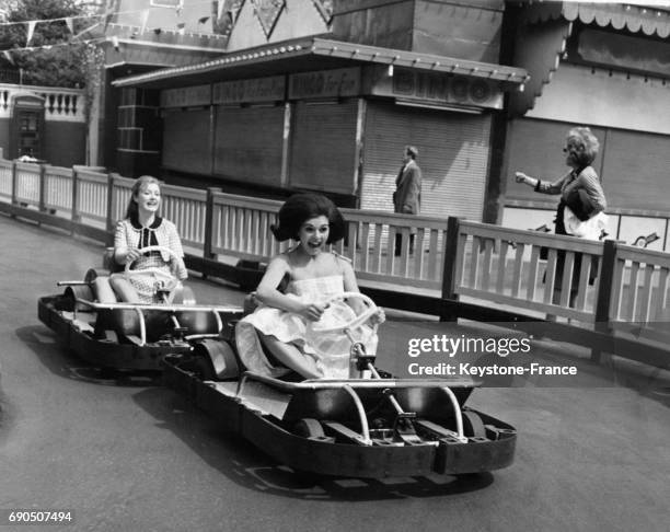 Les actrices Gloria Best et Suzanne Owens, cheveux au vent, sur la piste de karting à la fête foraire de Battersea, à Londres, Angleterre,...