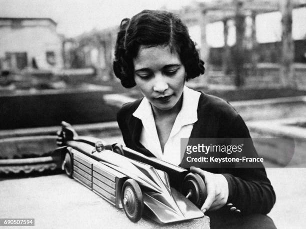 Une jeune fille tient dans ses mains une réplique miniature de la Golden Arrow, voiture ayant battu le record de vitesse en 1929, circa 1930.