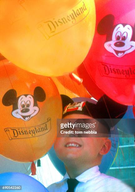 View of a young boy in a Mickey Mouse hat as he stands among a number of colorful balloons at Disneyland, Anaheim, California, January 1962.