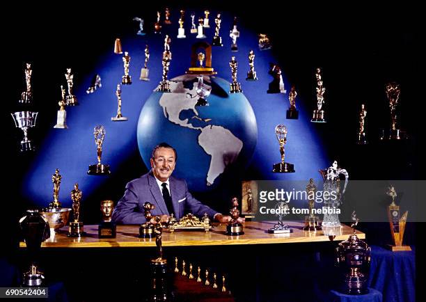 Portrait of American film producer and studio executive Walt Disney as he sits at his desk, Burbank, California, January 1963. A number of trophies,...