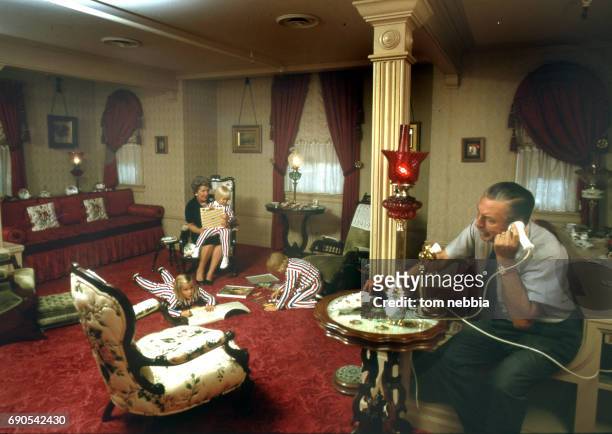 As American film producer and studio executive Walt Disney talks on the telephone, his wife, Lillian Disney , plays with three of their...