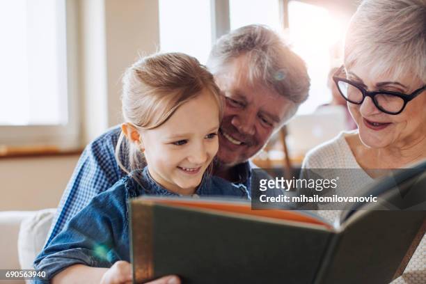 grandparents reading a book to their beautiful granddaughter - stories of the day stock pictures, royalty-free photos & images