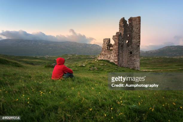 one man sitting near ardvreck castle, loch assynt, scotland. - in rovina foto e immagini stock