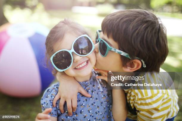 a brother and a sister, wearing sun glasses, posing together - kissing kids stockfoto's en -beelden