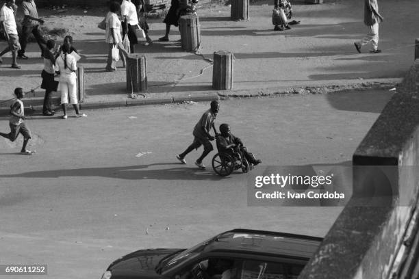 young  man carries a friend on a wheelchair in the centre of bujumbura, burundi. - eastern african tribal culture stock pictures, royalty-free photos & images