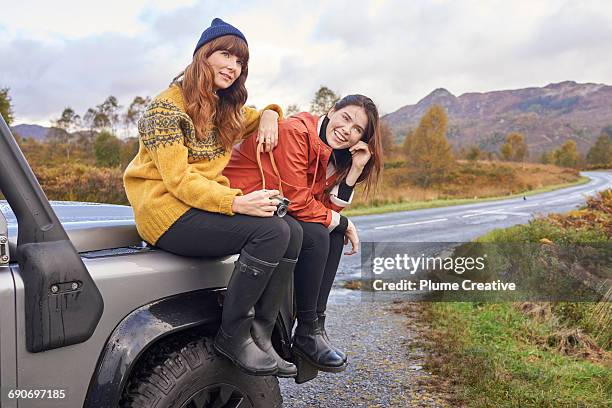 two friends on a road trip - sat on their car - motorhaube stock-fotos und bilder