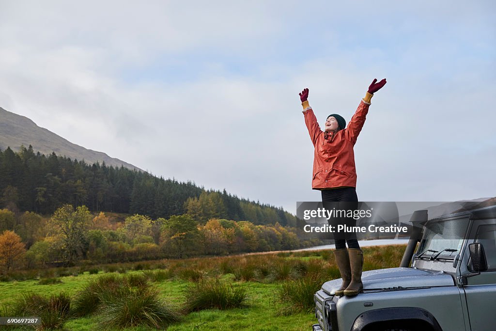 Woman with arms outstretched standing on car