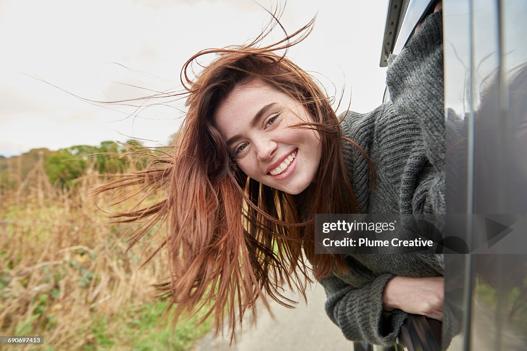 Young woman with head out of car window