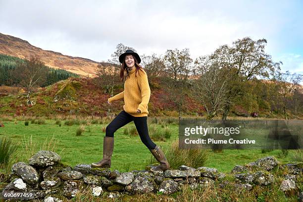 woman walking along stone wall - yellow boot stock pictures, royalty-free photos & images