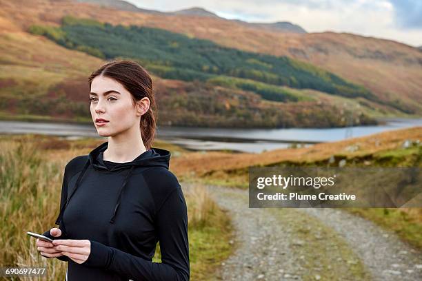 female runner taking a break - checking her phone - ropa de deporte fotografías e imágenes de stock