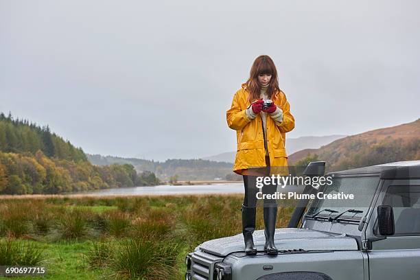 woman standing on car in beautiful landscape - laarzen geel stockfoto's en -beelden