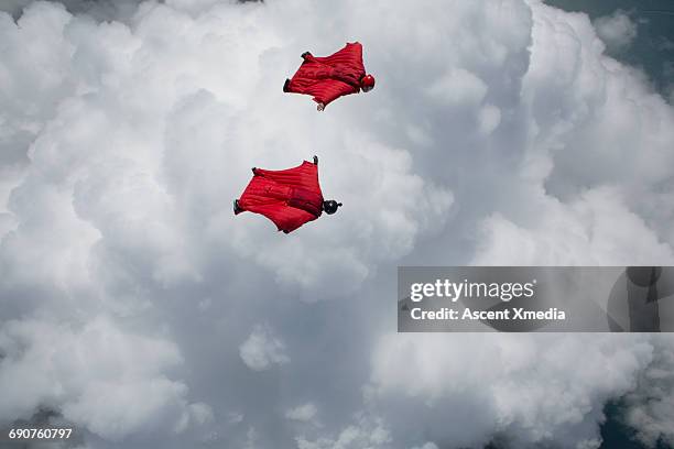 wingsuit fliers glide above clouds, mountains - aviation risk stock-fotos und bilder
