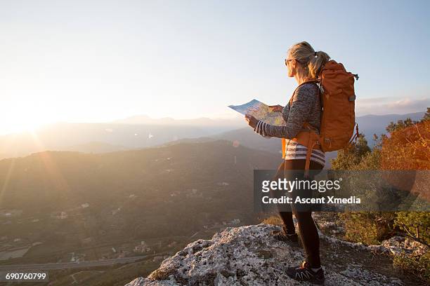 female hiker pauses to study map, hilly landscape - rucksack mit wanderschuhen stock-fotos und bilder