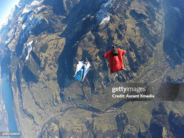wingsuit fliers glide above mountain landscape - wing suit stock pictures, royalty-free photos & images