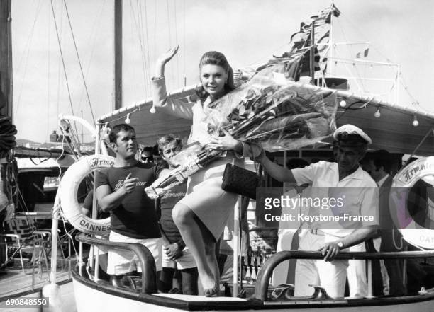 Actrice italienne Sylva Koscina salue depuis un bateau avec une gerbe de fleurs dans les bras.