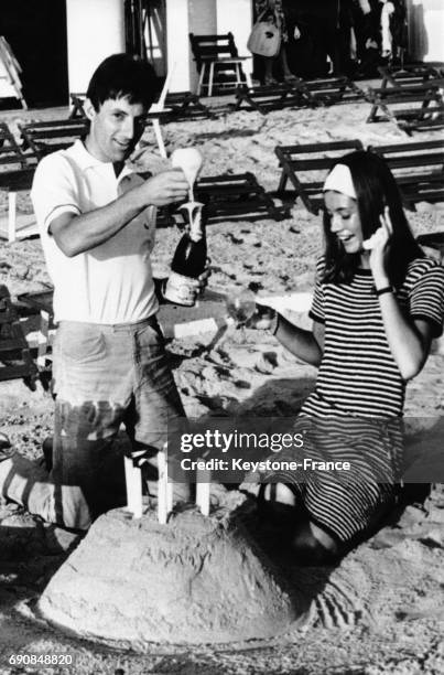 Françoise Hardy offrant à Hugues Aufray un gâteau de sable pour son anniversaire sur la plage à Juan-les-Pins, France, le 26 août 1964.