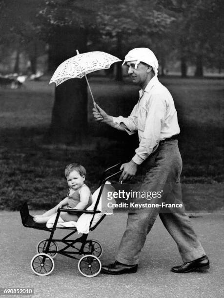 Un père promenant son enfant dans le poussette dans le jardin de Kensington à Londres, Royaume-Uni le 23 mai 1933.
