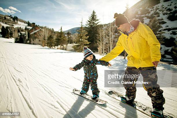 father holding his son during snowboard lesson. - atividades de fins de semana imagens e fotografias de stock