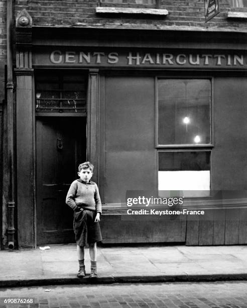 Un garçon londonien devant la devanture d'un salon de coiffure pour hommes dans Cable Street à Londres, Royaume-Uni.