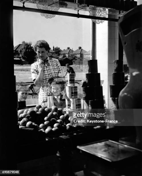 Travers la vitrine d'un magasin d'alimentation, une femme et son enfant regardent le prix des fruits, au Royaume-Uni.
